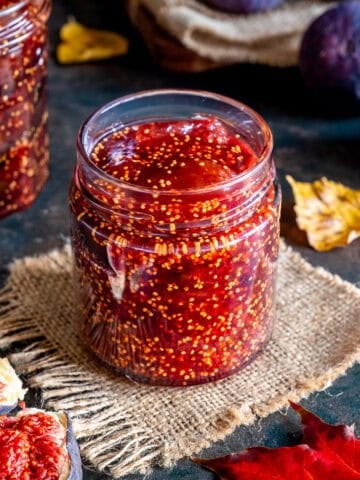 Homemade fig jam in a glass jar with fresh figs around.