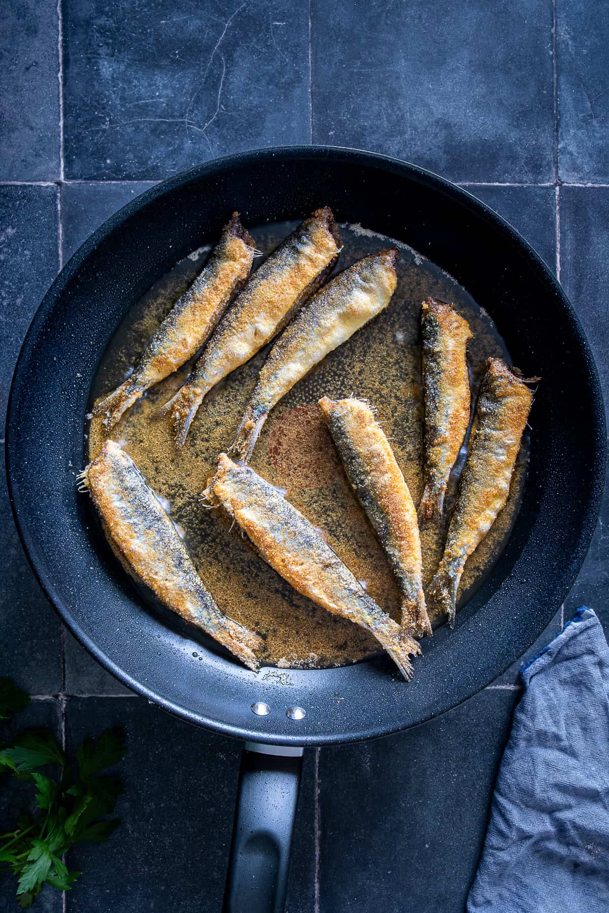 Golden fried sardines cooking in a skillet with oil.