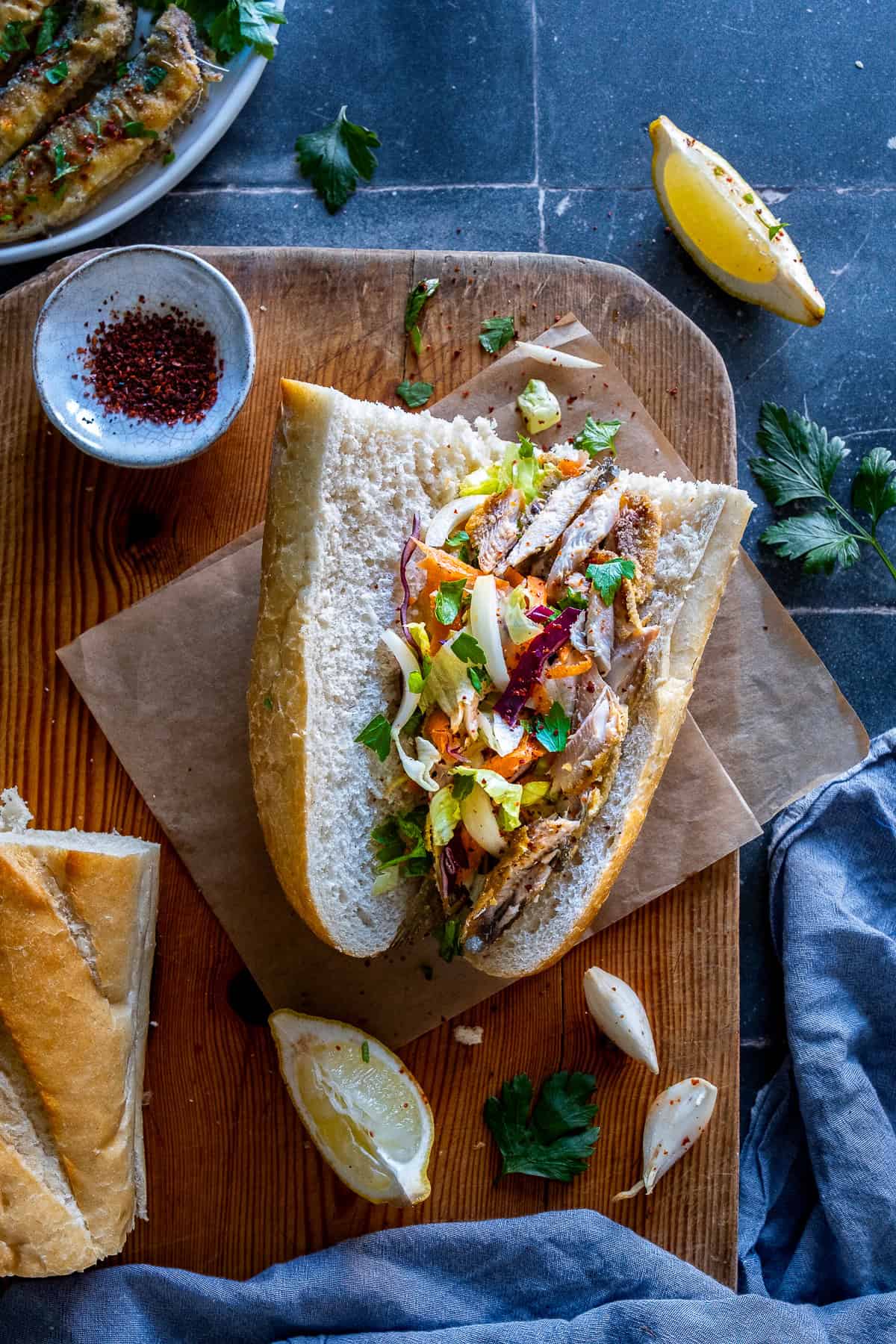 Fried sardine sandwich with mixed salad inside crusty bread, served with lemon and herbs.