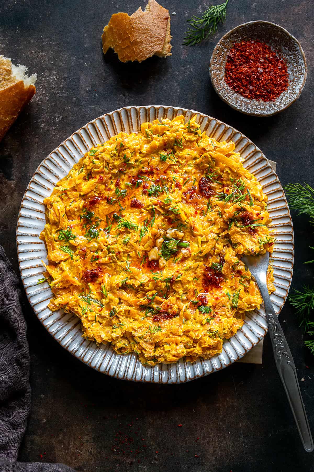 Overhead shot of Havuç Tarator on a plate, garnished with dill and chili oil, with bread pieces and pul biber on the side.