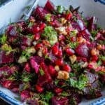 Turkish beet salad with tender beet chunks, herbs, walnuts, and pomegranate seeds in a white bowl.