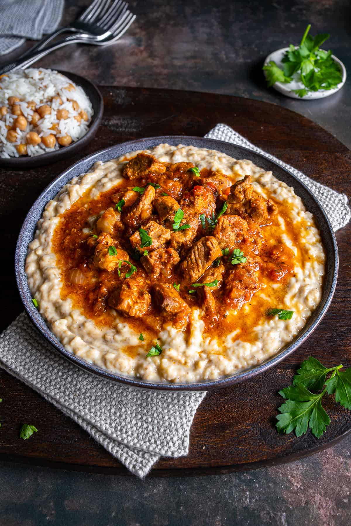 Hunkar Begendi served with tender lamb stew over creamy eggplant puree, garnished with parsley and served alongside rice.