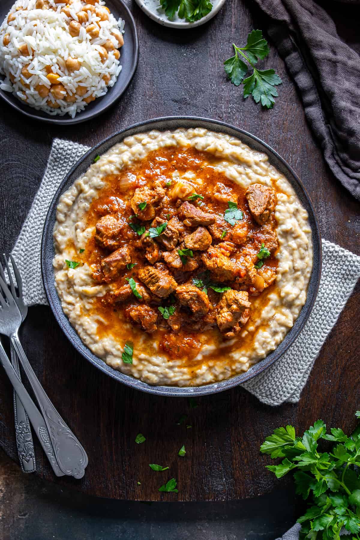 Overhead view of Hunkar Begendi with lamb stew served on creamy eggplant puree, garnished with parsley and accompanied by rice.