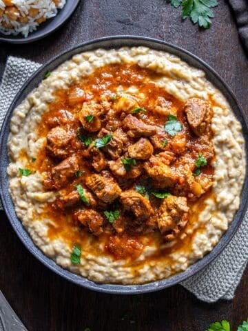 Hunkar Begendi with lamb stew served over creamy eggplant puree, garnished with parsley and served with rice.