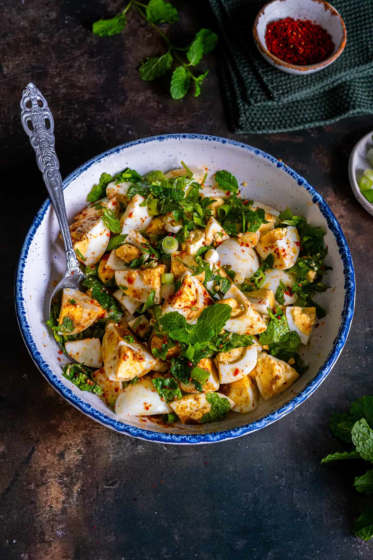 Overhead view of Turkish egg salad with boiled eggs, fresh herbs, and spices in a white bowl with a spoon.