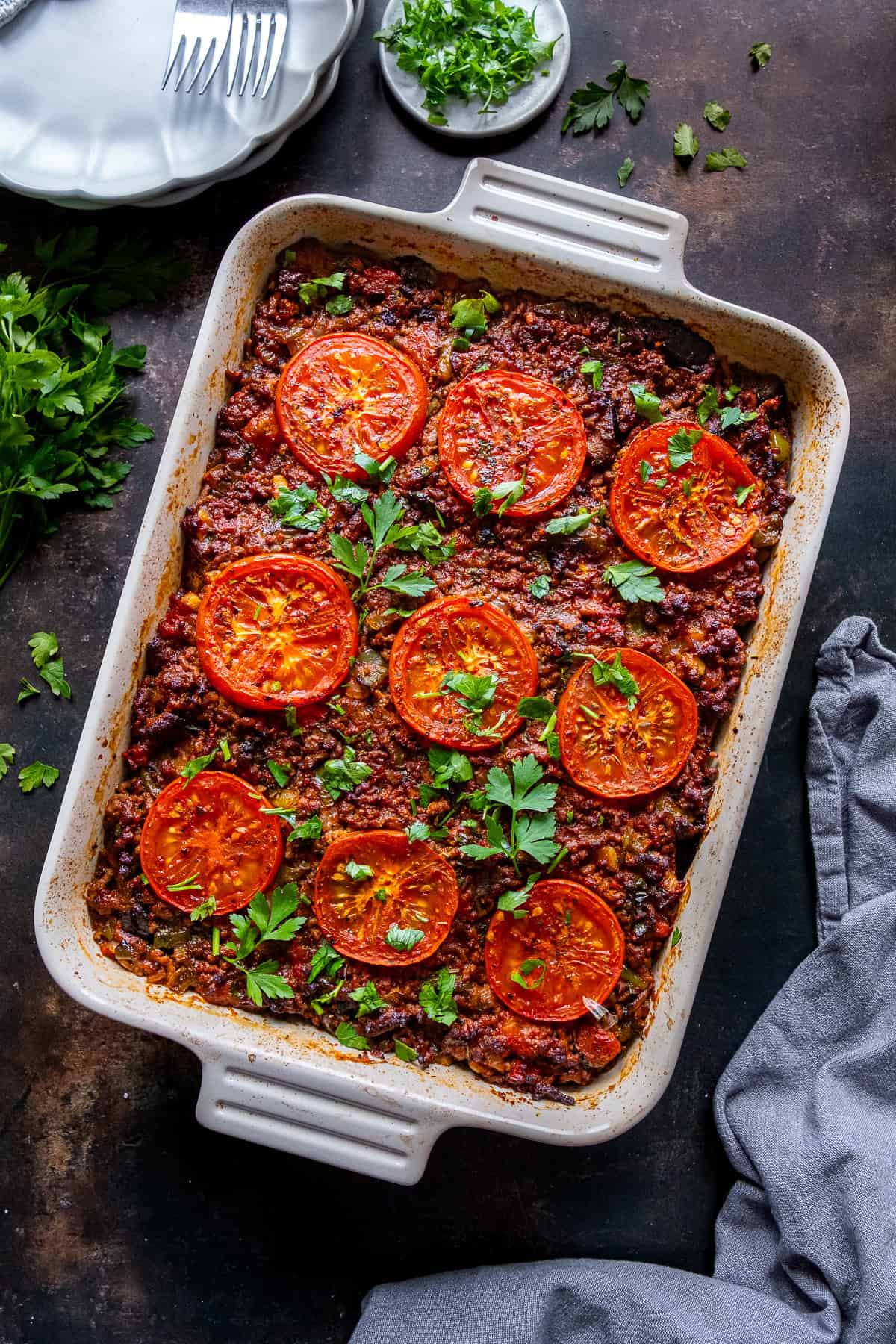 Baked Turkish moussaka in a casserole dish topped with roasted tomato slices and fresh parsley.