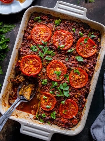 Featured image of Turkish moussaka baked in a casserole dish with roasted tomato slices and fresh parsley on top.