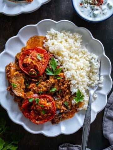 Overhead view of Turkish moussaka with roasted eggplant and ground beef served with rice pilaf and cacık on the side.