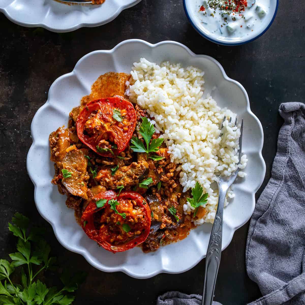 Overhead view of Turkish moussaka with roasted eggplant and ground beef served with rice pilaf and cacık on the side.
