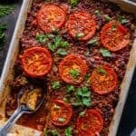 Pinterest image for Turkish moussaka showing baked eggplant and ground beef topped with roasted tomato slices and parsley.