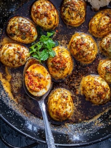 Close-up of hard-boiled eggs in spiced butter with dried mint and Turkish red pepper flakes.
