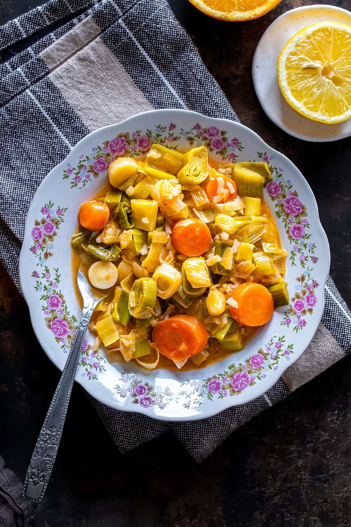 Turkish Leeks in Olive Oil with carrots and rice, served on a floral plate with lemon slices on the side.