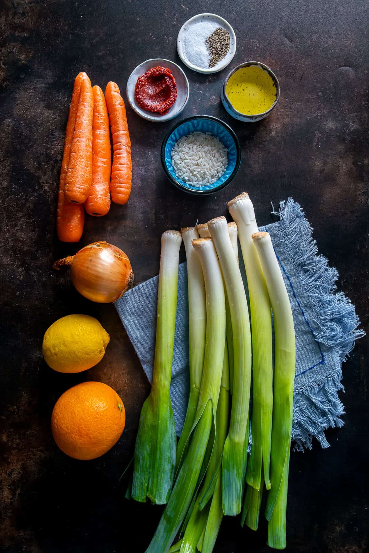 Ingredients for Turkish Leeks in Olive Oil including fresh leeks, carrots, onion, rice, olive oil, tomato paste, lemon, and orange.