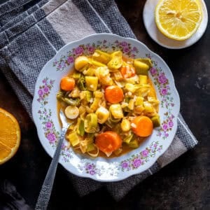 Close overhead view of Turkish Leeks in Olive Oil with carrots and rice served on a floral plate, with lemon halves and a folded kitchen towel nearby.