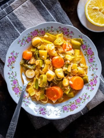 Close overhead view of Turkish Leeks in Olive Oil with carrots and rice served on a floral plate, with lemon halves and a folded kitchen towel nearby.