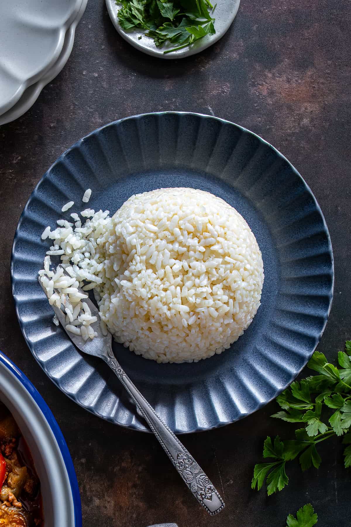 Overhead view of a dome-shaped serving of Turkish rice pilaf with fluffy, separate grains on a dark blue plate, with a fork on the side.