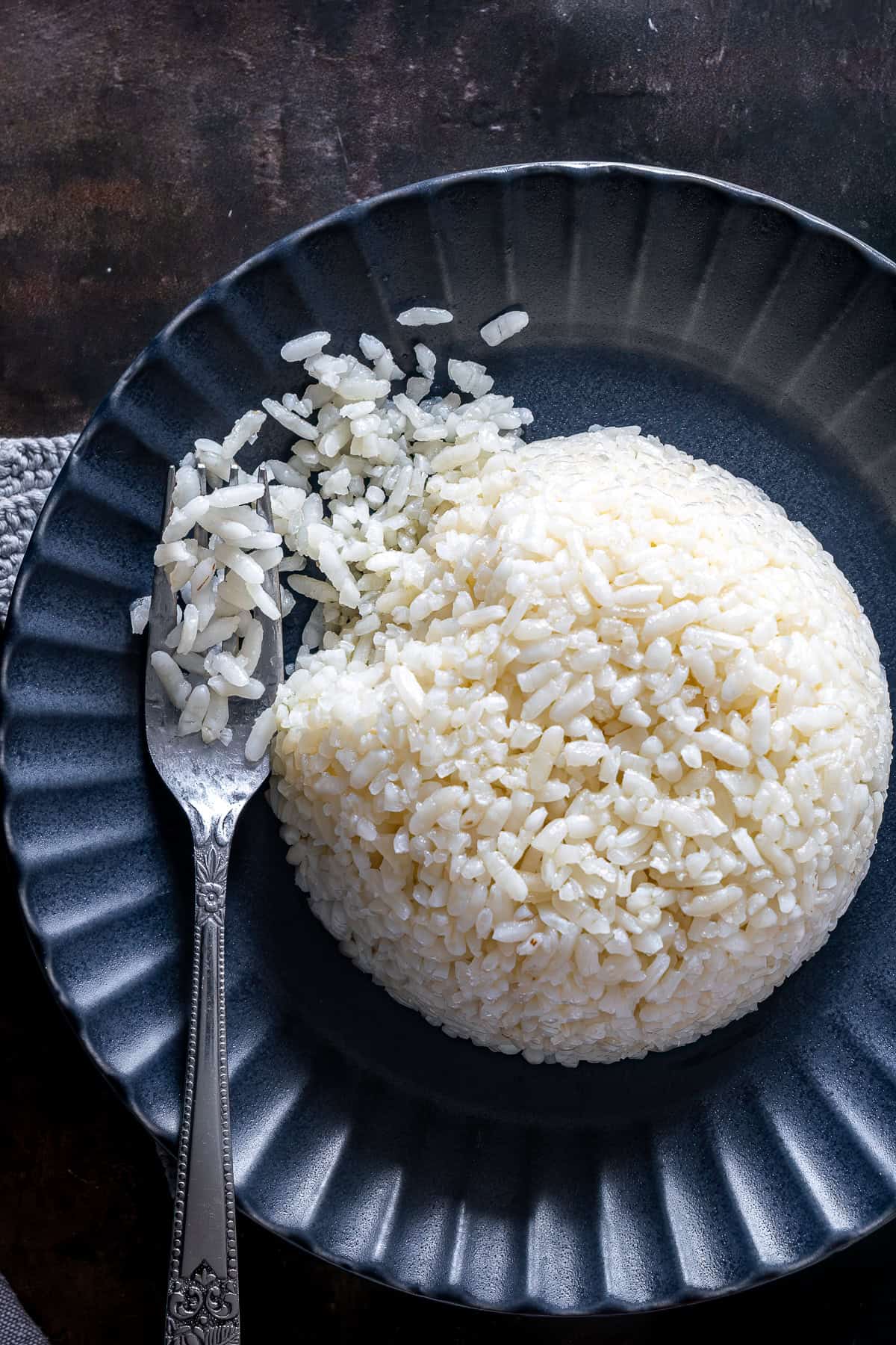Close-up of fluffy Turkish rice pilaf shaped into a dome on a dark plate, with a fork lifting separate grains.