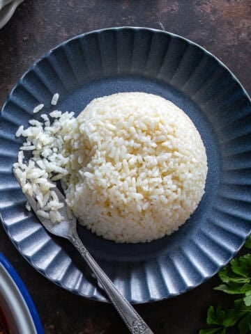 Overhead view of fluffy Turkish rice pilaf shaped into a dome on a dark blue plate, with a fork lifting separate grains.