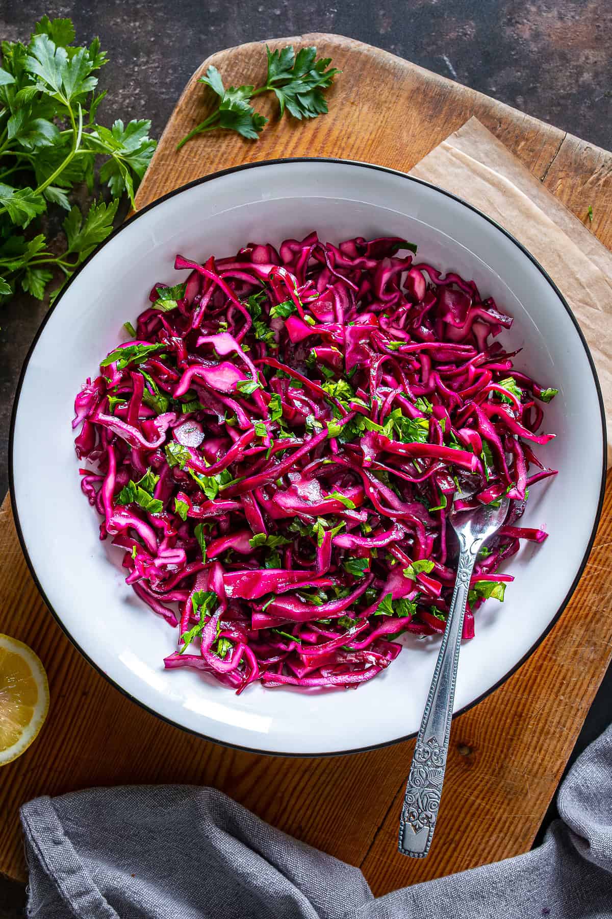 Thinly sliced Turkish red cabbage salad with parsley and lemon in a white bowl on a wooden board.