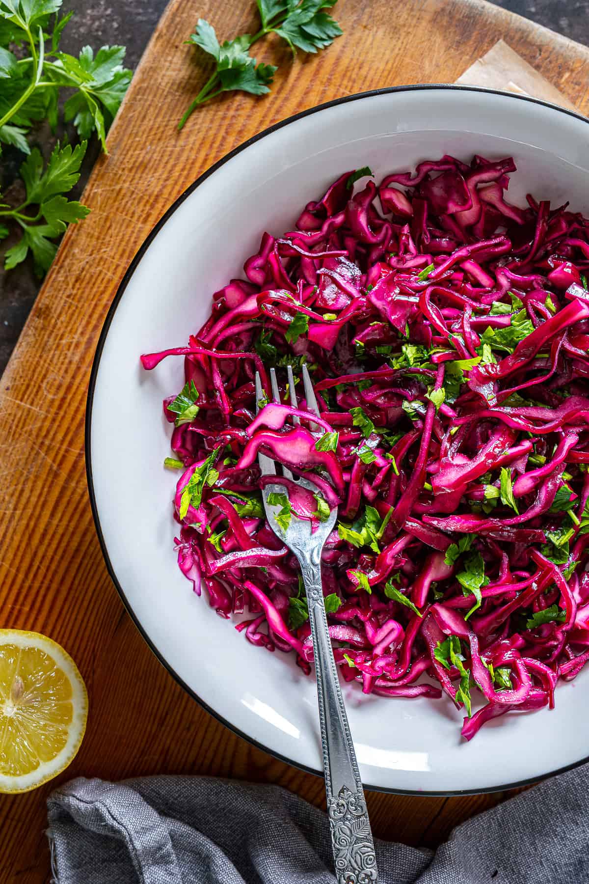 Close-up of Turkish red cabbage salad with parsley and lemon in a white bowl on a wooden board.