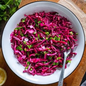 Thinly sliced Turkish red cabbage salad with parsley, lemon, and olive oil in a white bowl.