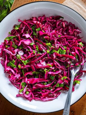 Thinly sliced Turkish red cabbage salad with parsley, lemon, and olive oil in a white bowl.