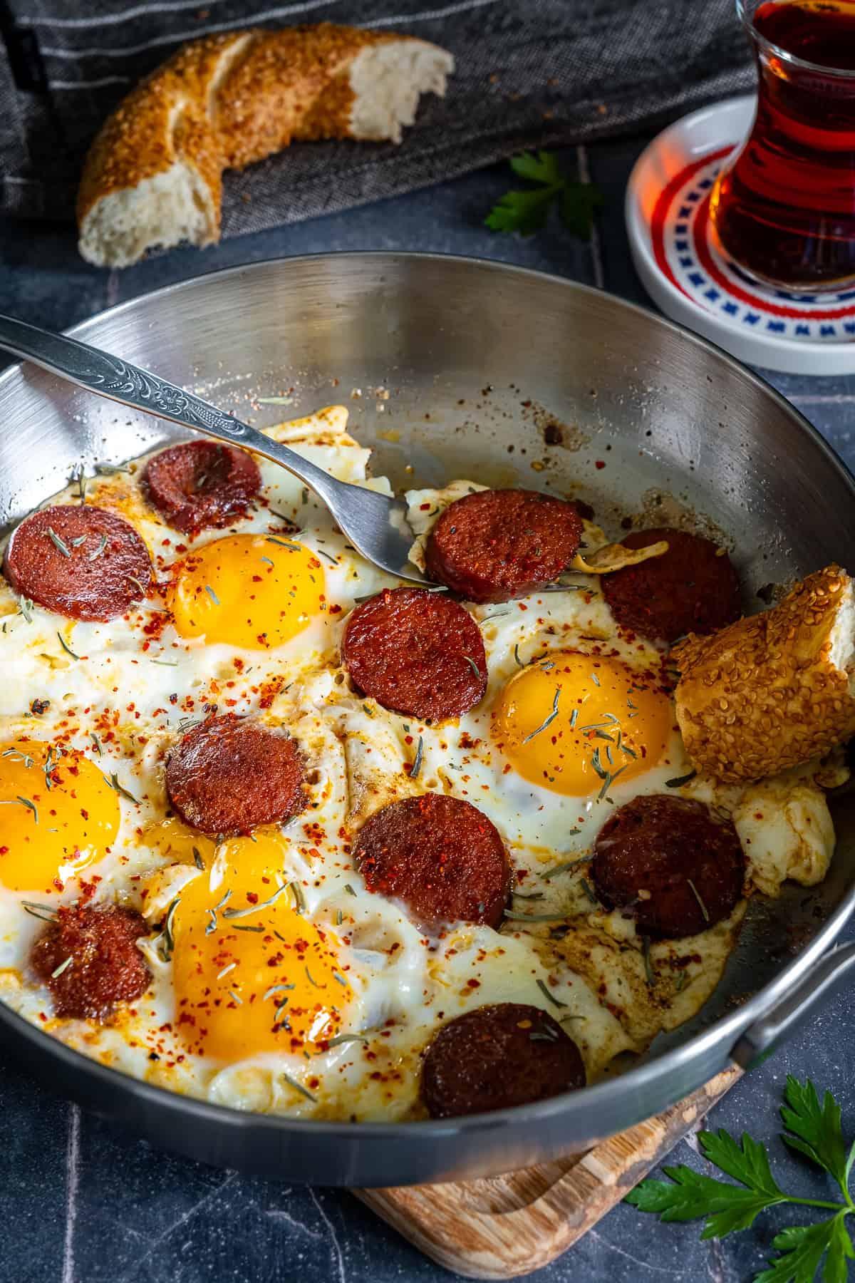 Turkish sucuk and eggs served in a pan with simit and Turkish tea on the side.