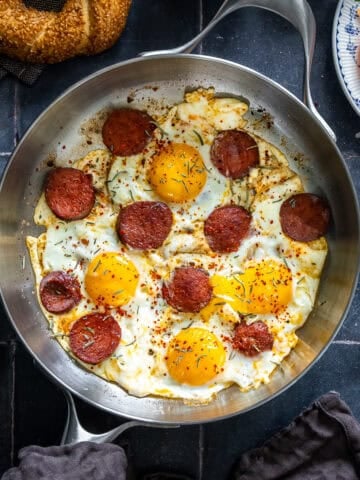 Overhead view of Turkish sucuk and eggs cooked in a pan and served with simit and tomatoes for breakfast.