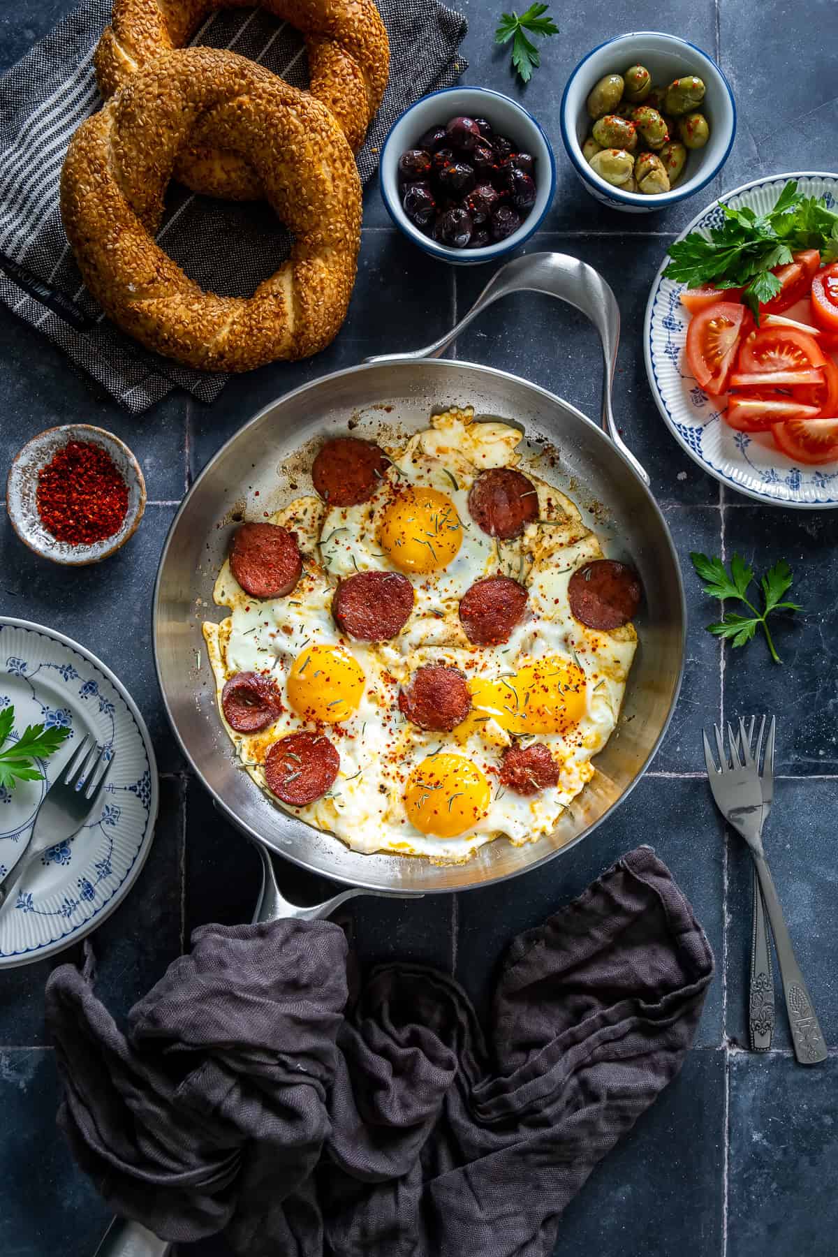 Turkish sucuk and eggs served in a pan with simit, olives, tomatoes, and Turkish tea for a traditional Turkish breakfast spread.