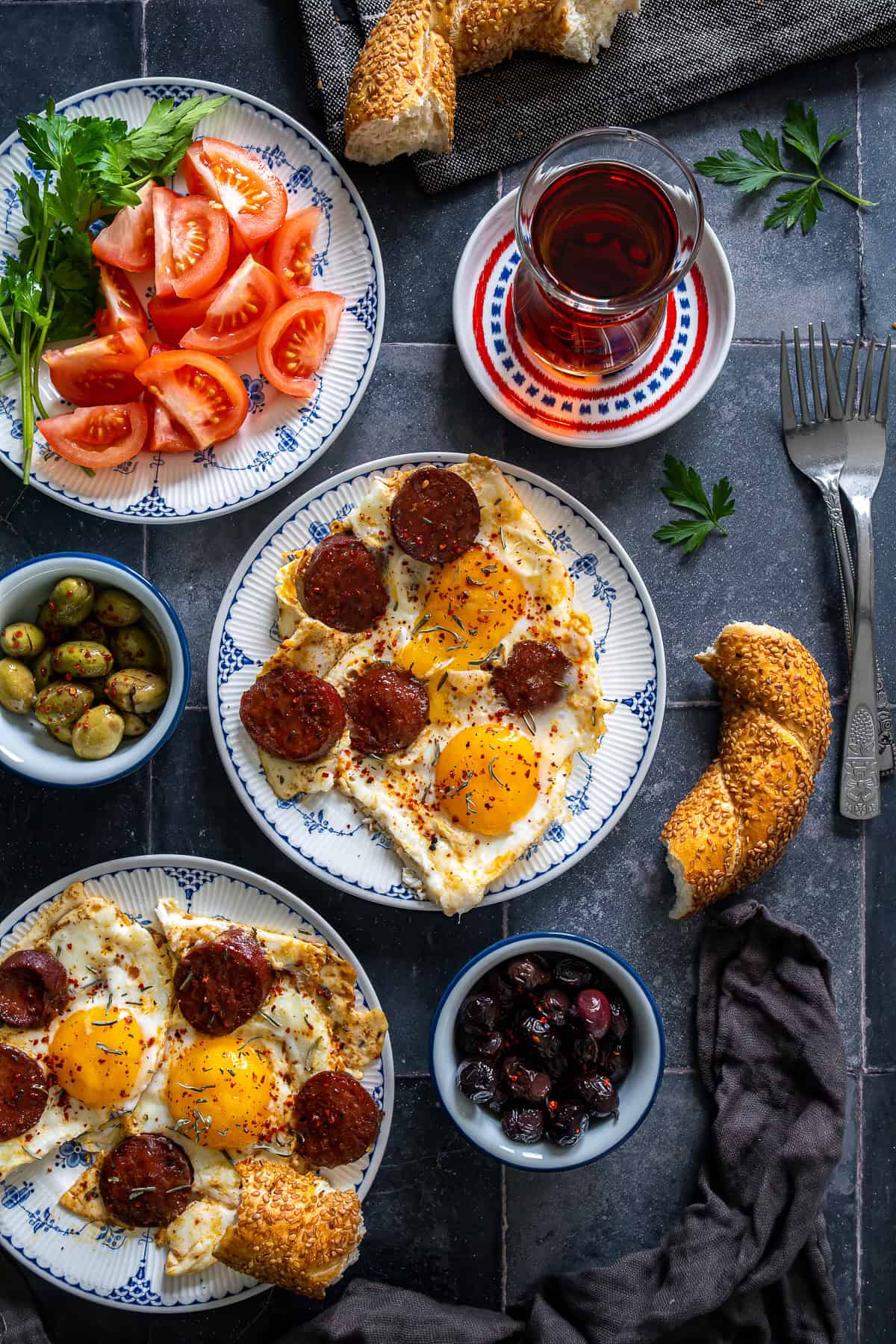 Turkish sucuk and eggs served with simit, olives, tomatoes, and Turkish tea for a traditional weekend breakfast spread.