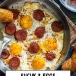 Turkish sucuk and eggs served in a pan with simit and sliced tomatoes on the side.
