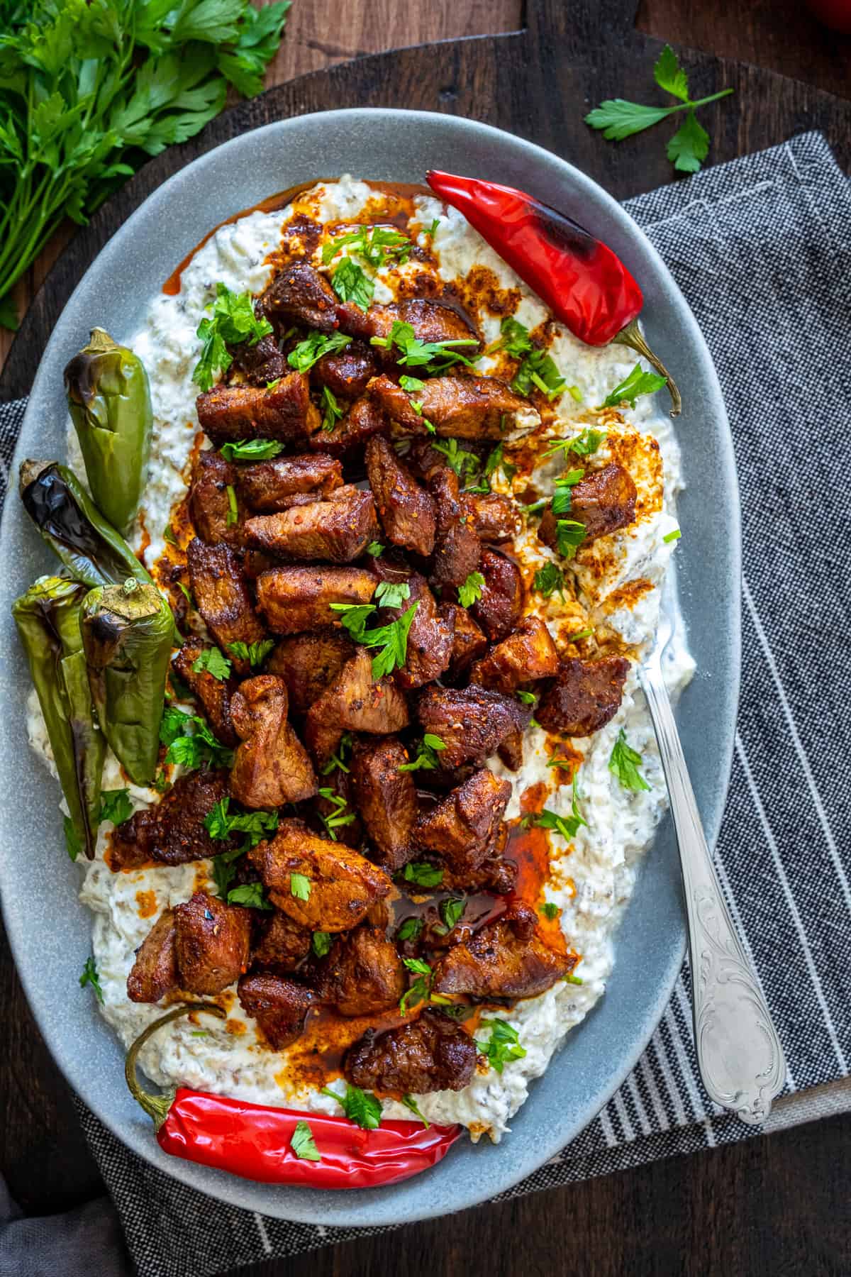 Ali Nazik Kebab served on a gray oval plate with roasted peppers, chopped parsley, and a fork inside.