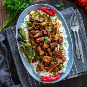 Ali Nazik Kebab served on a gray oval plate with roasted peppers, fresh parsley, and forks on the side.