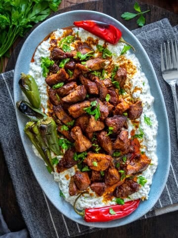 Ali Nazik Kebab served on a gray oval plate with roasted peppers, fresh parsley, and forks on the side.