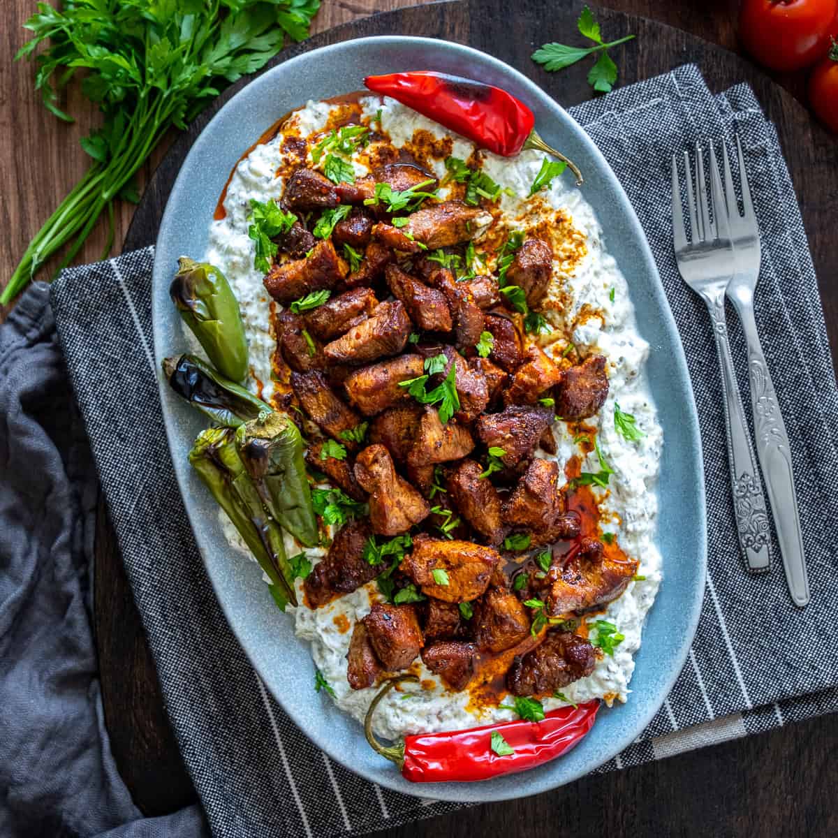 Ali Nazik Kebab served on a gray oval plate with roasted peppers, fresh parsley, and forks on the side.