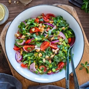 Turkish purslane salad with fresh purslane, cherry tomatoes, red onion and walnuts in a tangy pomegranate molasses dressing, served in a white bowl.