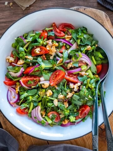 Turkish purslane salad with fresh purslane, cherry tomatoes, red onion and walnuts in a tangy pomegranate molasses dressing, served in a white bowl.