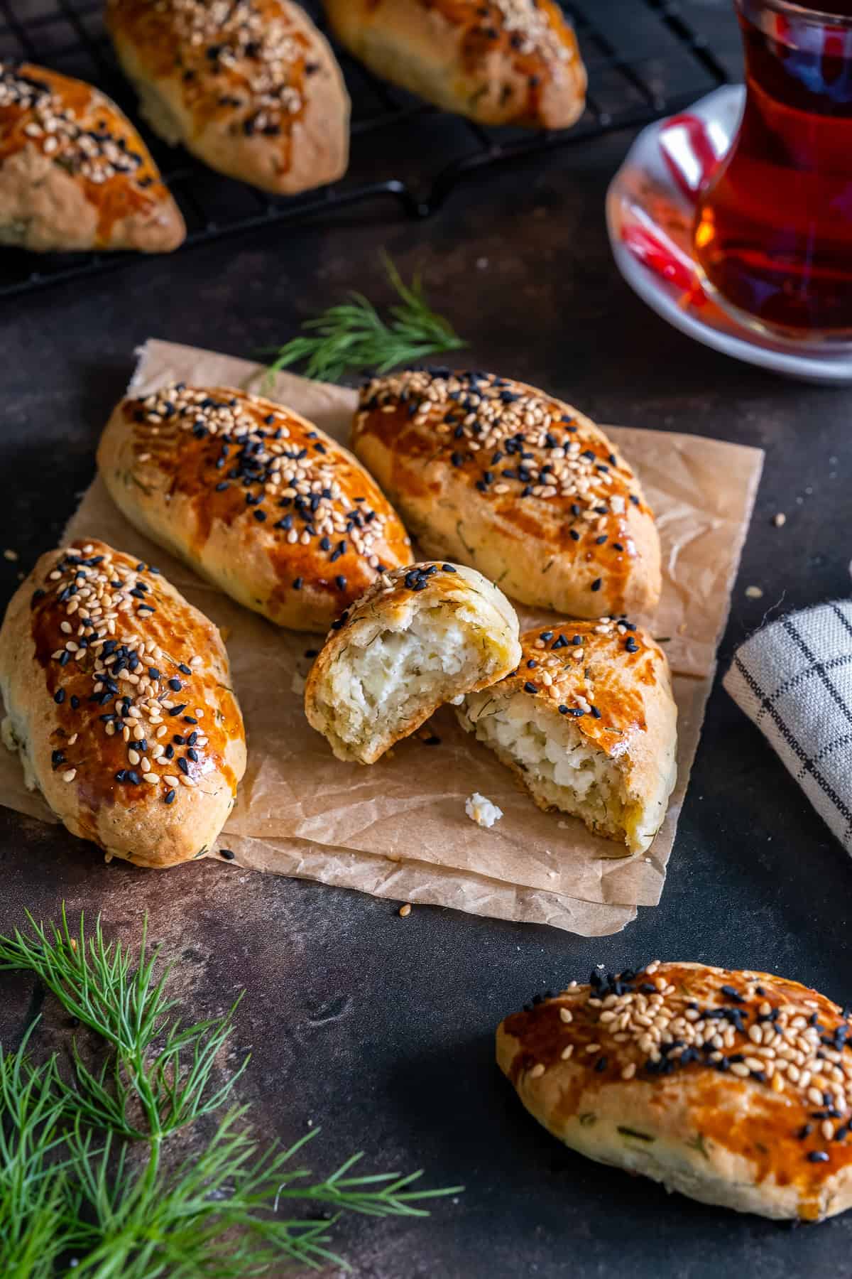 Turkish pogaca with dill (dereotlu pogaca) topped with sesame and nigella seeds, with one pastry halved to show the cheese filling, served with Turkish tea.