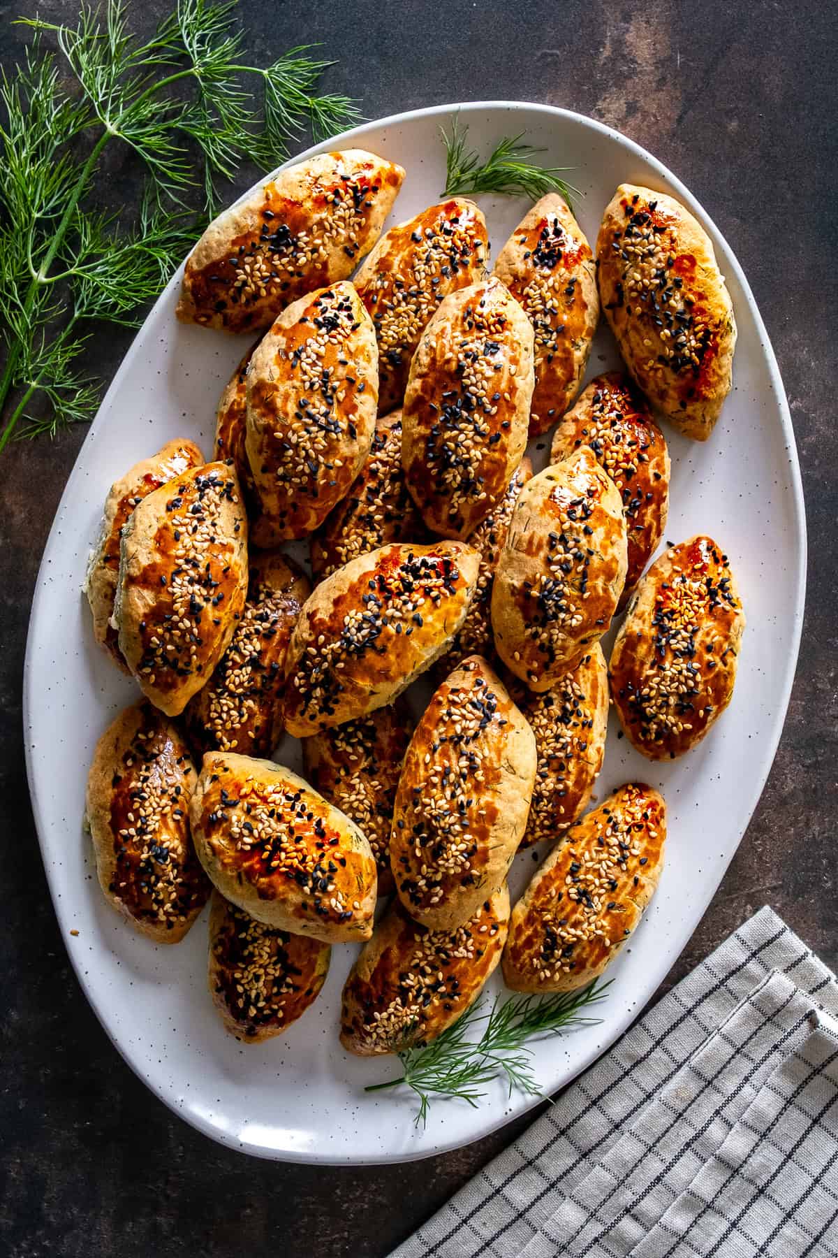 A platter of freshly baked Turkish pogaca with dill (dereotlu pogaca) topped with sesame and nigella seeds, garnished with fresh dill.