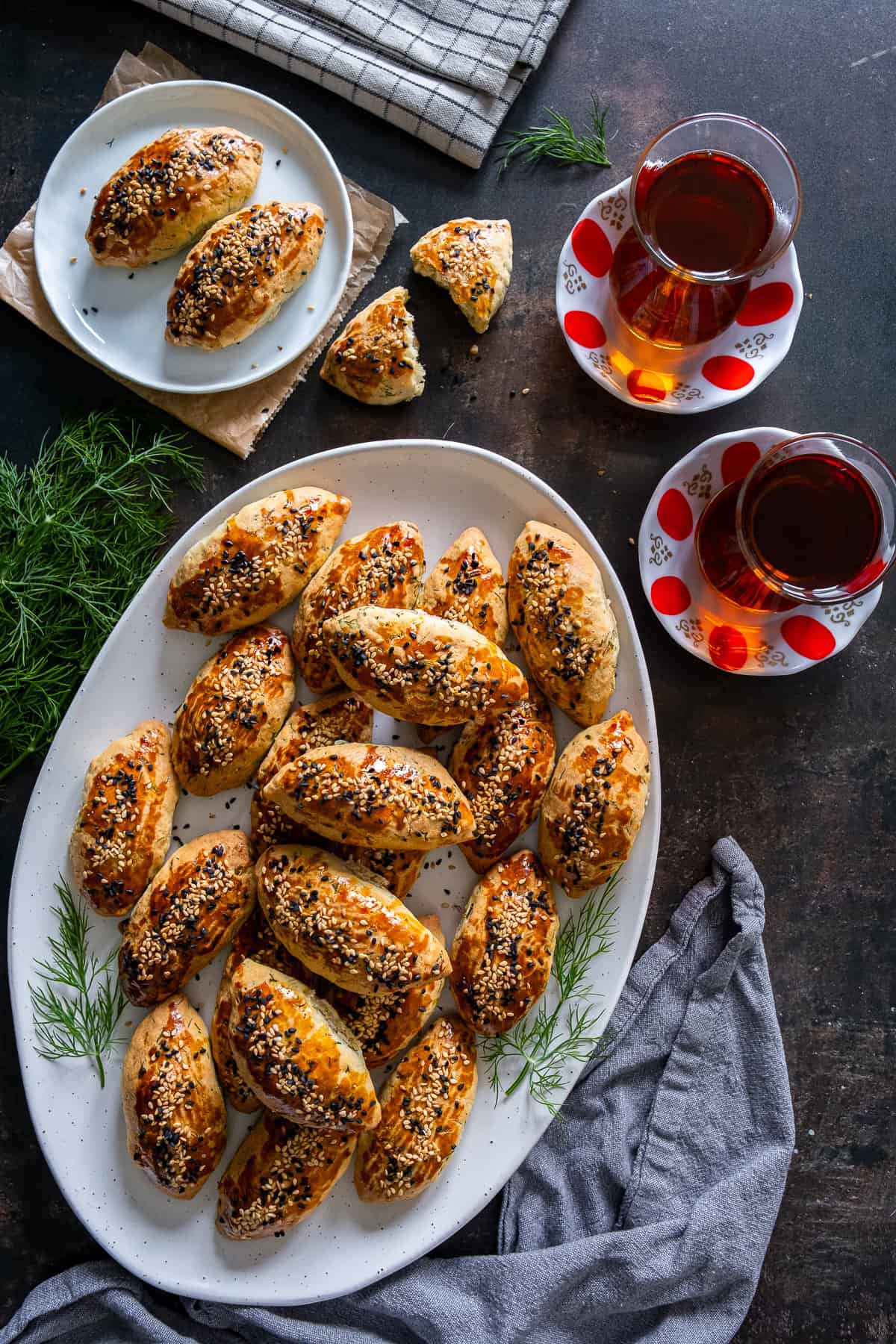 Overhead picture of Turkish pogaca with dill (dereotlu pogaca) served on a platter with two glasses of Turkish tea on the side.