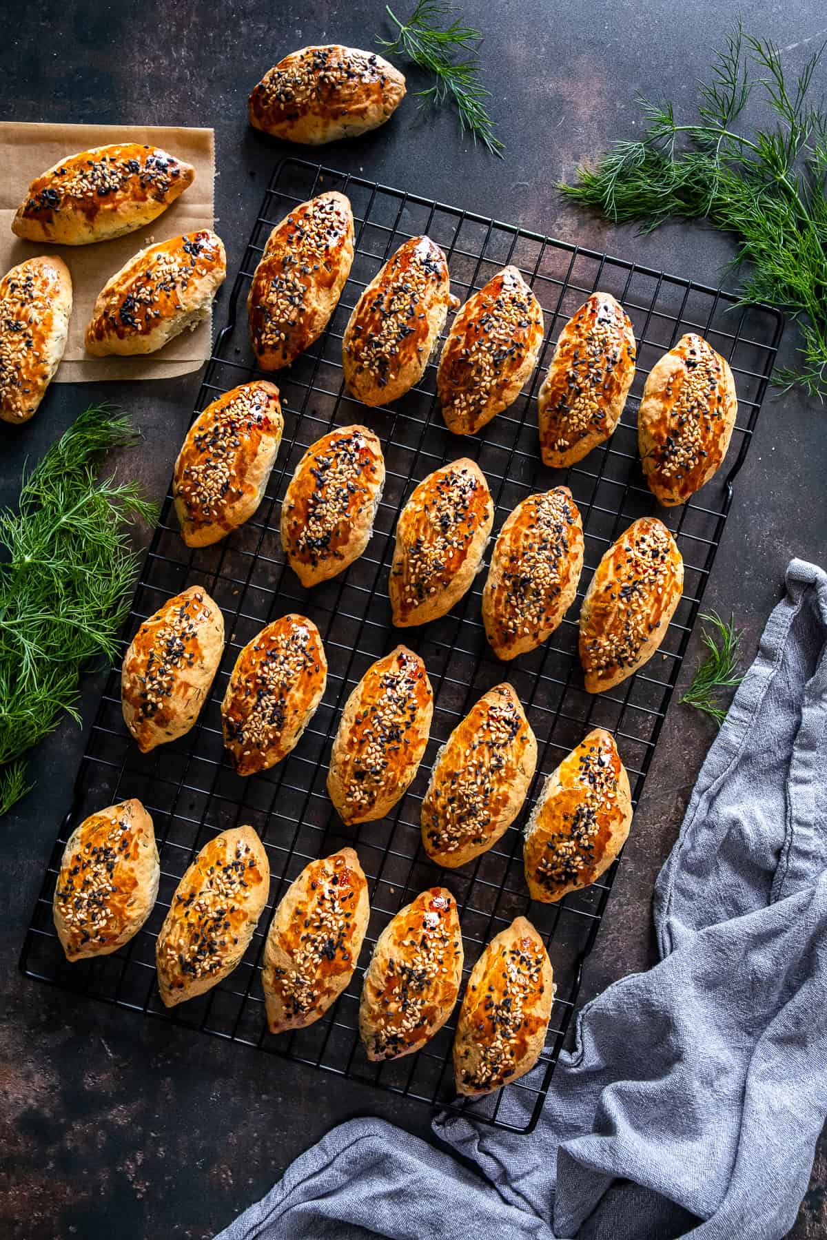 Freshly baked Turkish pogaca with dill (dereotlu pogaca) topped with sesame and nigella seeds, cooling on a wire rack.