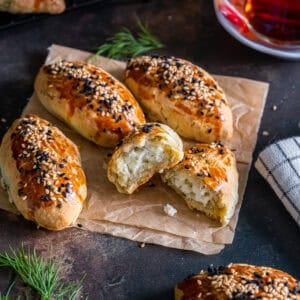 Turkish pogaca with dill (dereotlu pogaca), with one pastry halved open to show the cheese filling, topped with sesame and nigella seeds, served with Turkish tea.