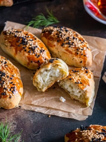 Turkish pogaca with dill (dereotlu pogaca), with one pastry halved open to show the cheese filling, topped with sesame and nigella seeds, served with Turkish tea.