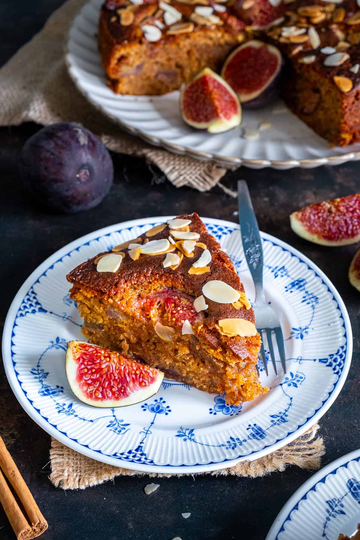 Slice of fresh fig cake with a soft, moist crumb, topped with flaked almonds and served with fresh figs.