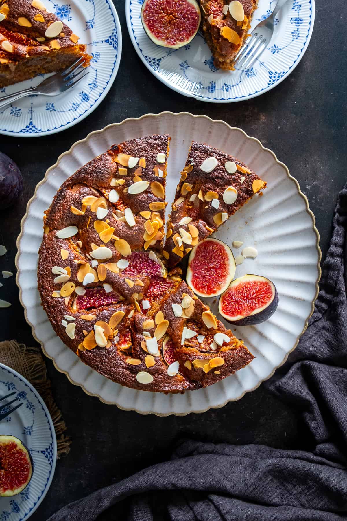 Sliced fresh fig cake topped with baked figs and flaked almonds, with slices served on plates.