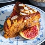 Fresh fig cake with a thick, moist crumb and baked figs inside, topped with flaked almonds and served with a fresh fig half.