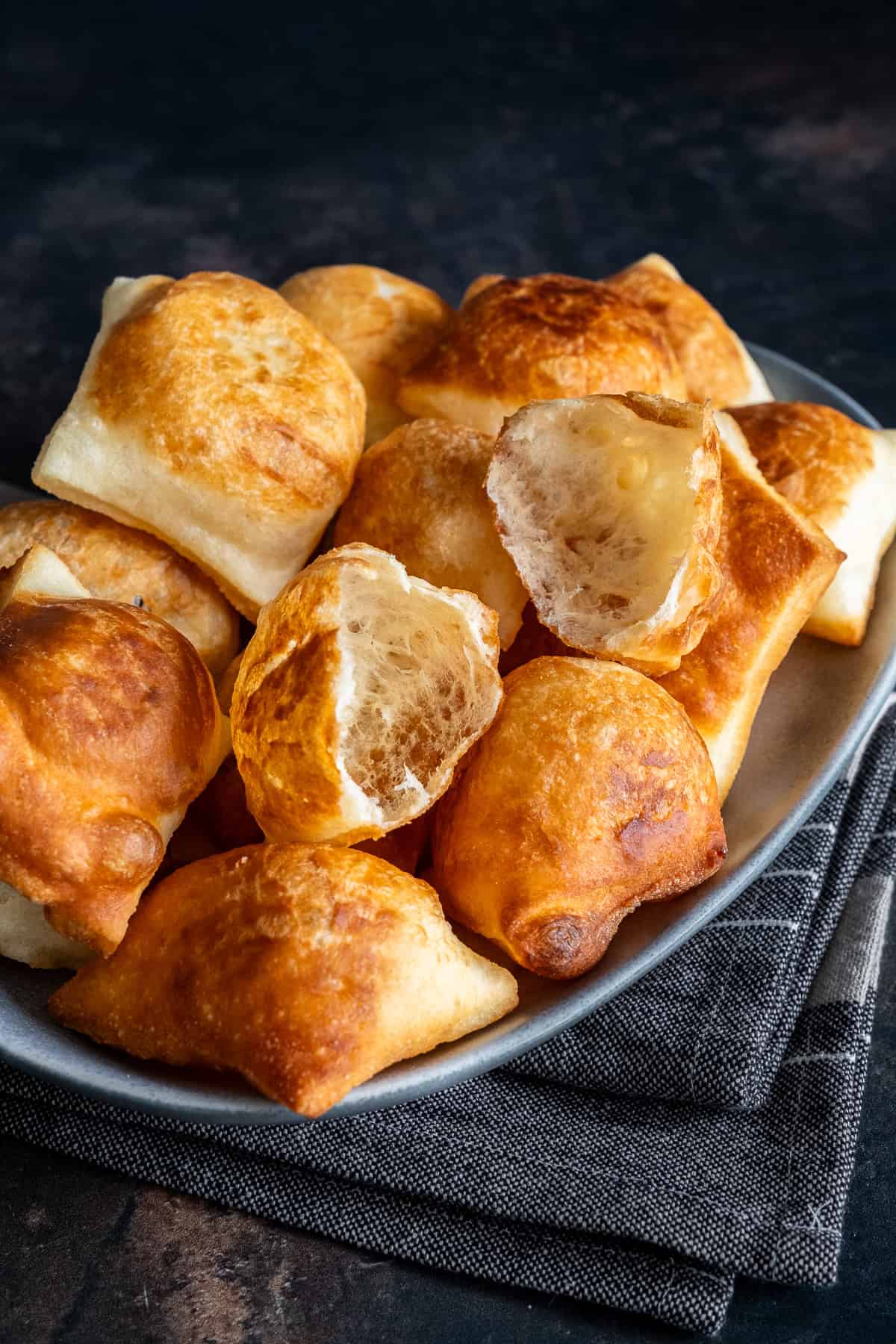 Plate of golden, puffy Turkish pişi, with two pieces torn open to show the soft, airy inside.