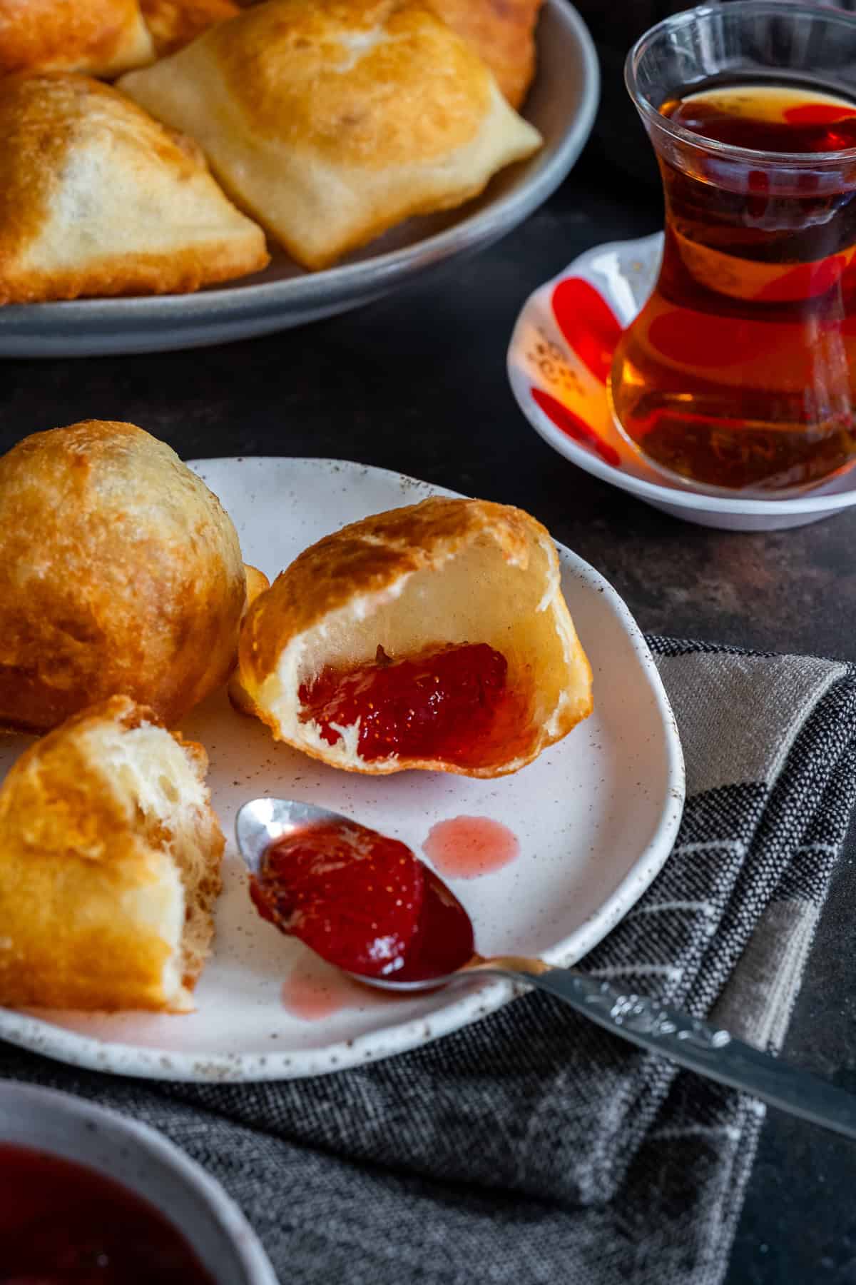 Golden Turkish pişi torn open and filled with strawberry jam, served with a glass of Turkish tea.