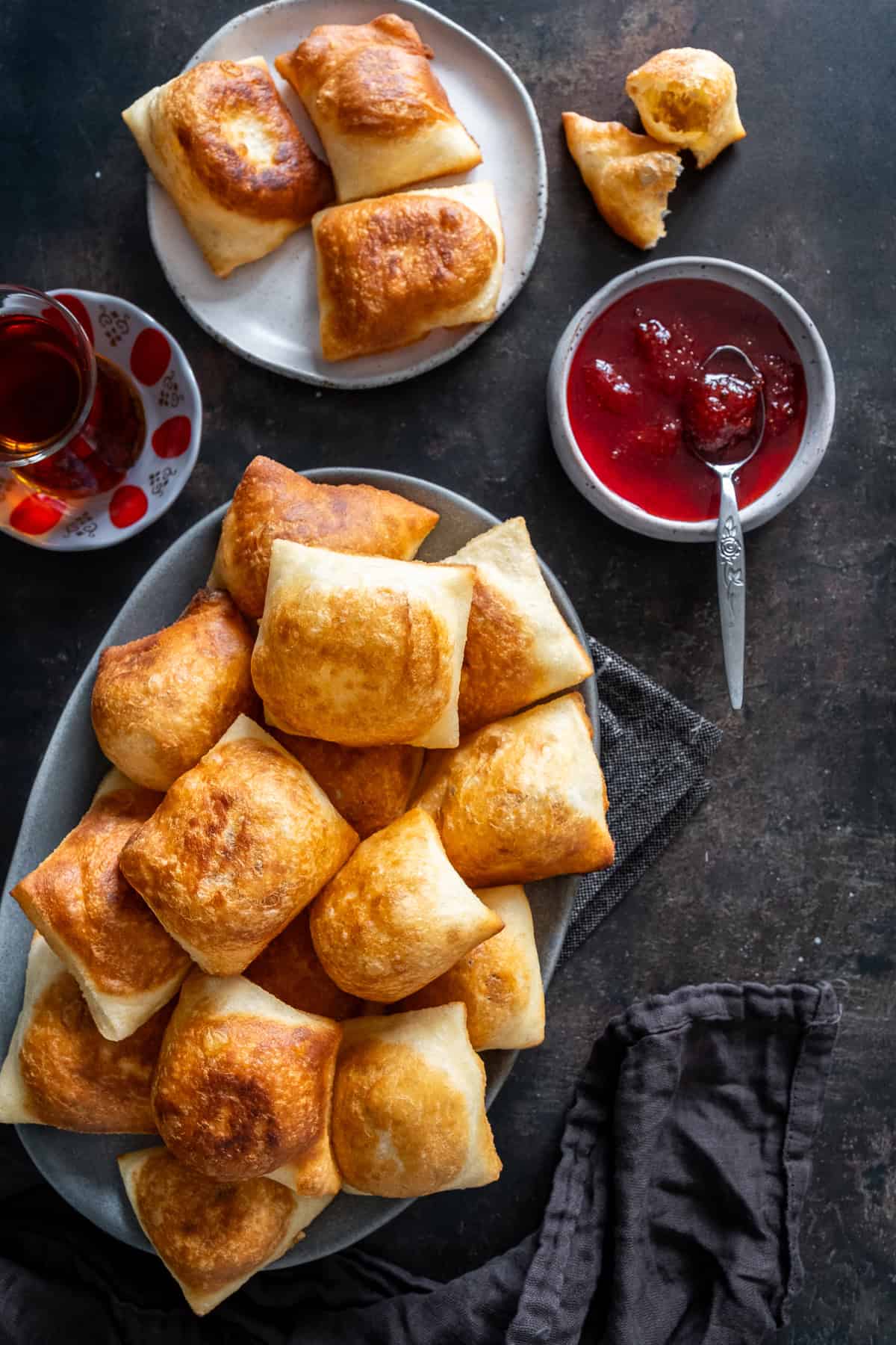 Platter of golden, puffy Turkish pişi served with strawberry jam and a glass of Turkish tea.