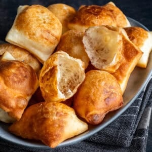 Close-up of golden, puffy Turkish pişi, with two torn open to show their light and airy inside.